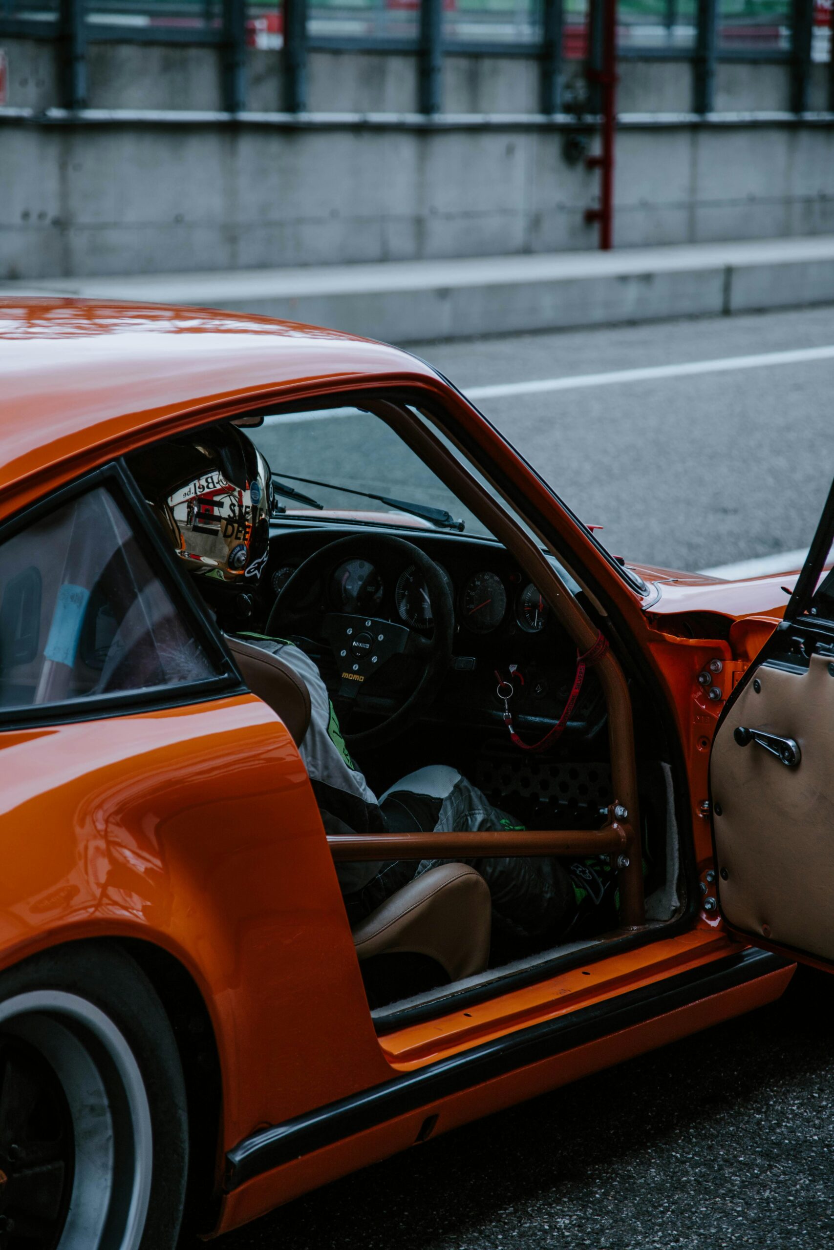 A vibrant orange race car parked at the pit lane with a driver seated inside.